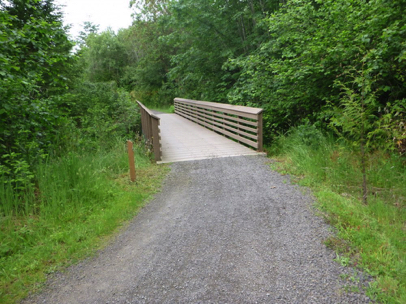 Foot bridge with a transition from compacted gravel to hard surface of composite boards